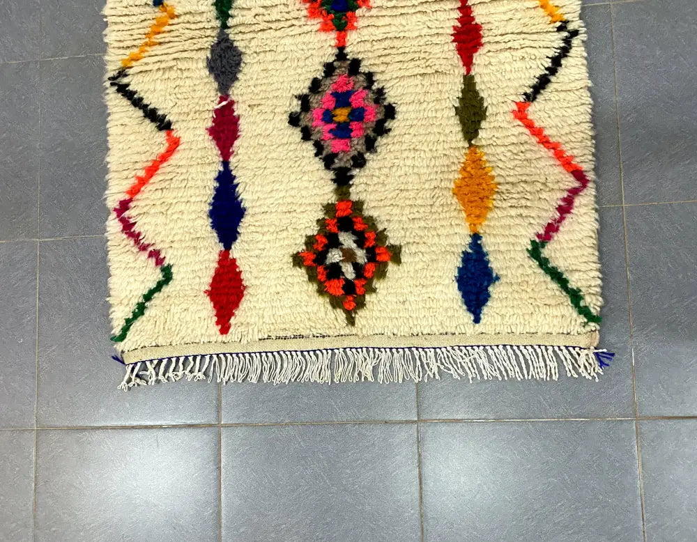 Cream-colored decorbites™ moroccan handmade azilal rug 1.5m x 1m with vibrant geometric patterns on textured woolen surface