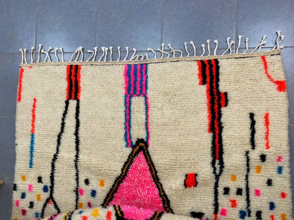 Cream-colored moroccan handmade azilal rug with bold pink red blue and black geometric patterns and fringed edge