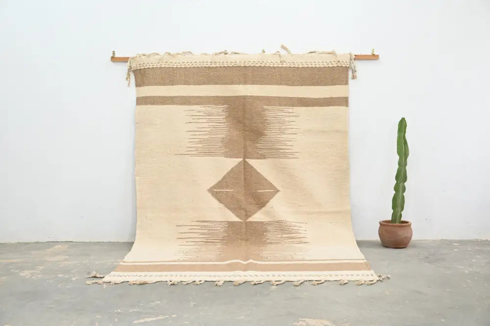 Beige and tan geometric-patterned moroccan handmade azilal rug with fringed edges hanging on wooden rod 300x200cm