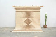 Beige and tan geometric-patterned moroccan handmade azilal rug with fringed edges hanging on wooden rod 300x200cm