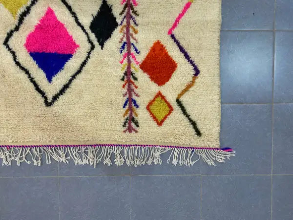 Cream-colored moroccan handmade azilal rug with bold geometric patterns and purple fringe in 3m by 2m size