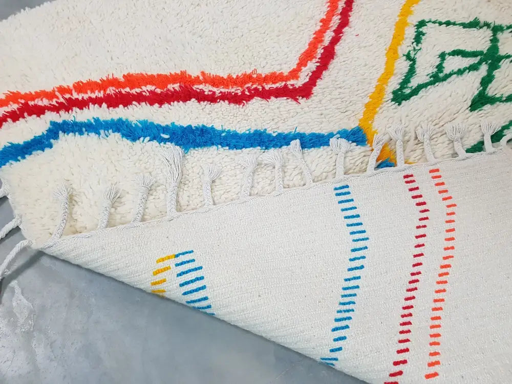 A plush white moroccan handmade azilal berber carpet with vibrant red blue green stripes and tassels supporting sustainable practices