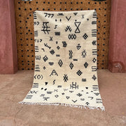 Cream-colored beni ouarain moroccan handmade carpet with black geometric patterns and fringed edges 2.5m x 1.5m