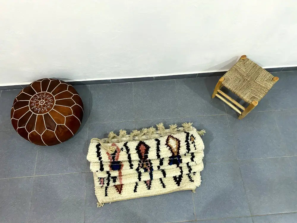 Brown leather moroccan pouf with white stitched geometric patterns complementing beni ouarain rug decorbites™ handmade design