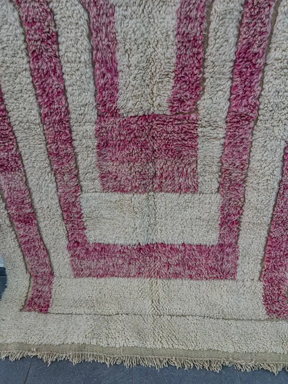 A plush cream-colored moroccan handmade beni ouarain rug with bold magenta geometric stripes and fringed edge