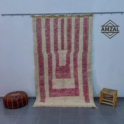 A plush cream and dusty rose striped moroccan handmade beni ouarain carpet with fringed edge hanging against the wall