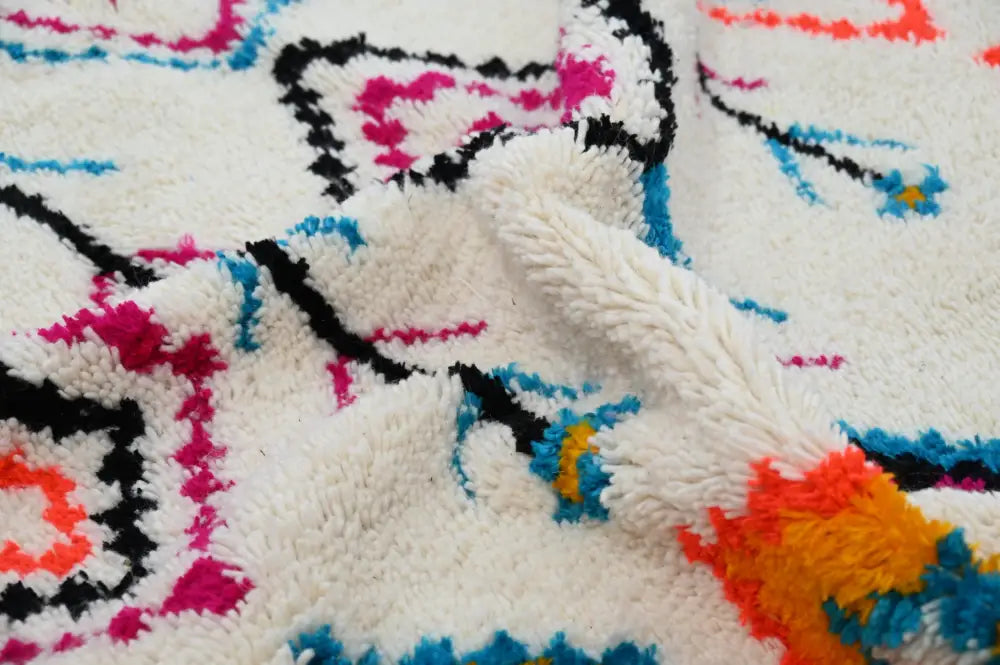 A cream-colored moroccan handmade traditional azilal carpet with vibrant abstract patterns in black pink blue orange and yellow