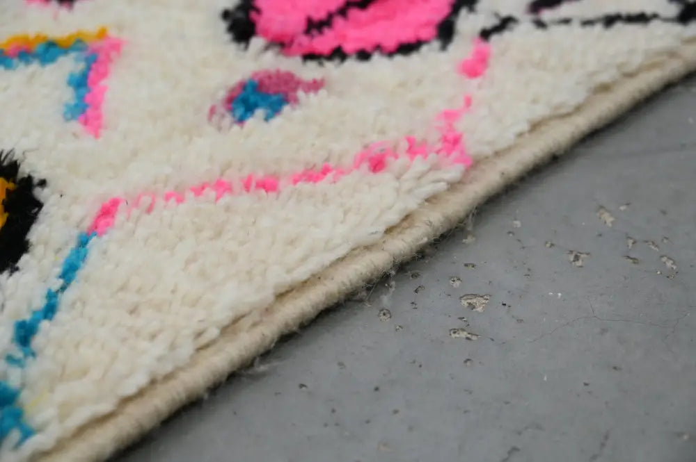 A moroccan handmade azilal hallway rug with vibrant pink blue and black geometric patterns on an off-white base