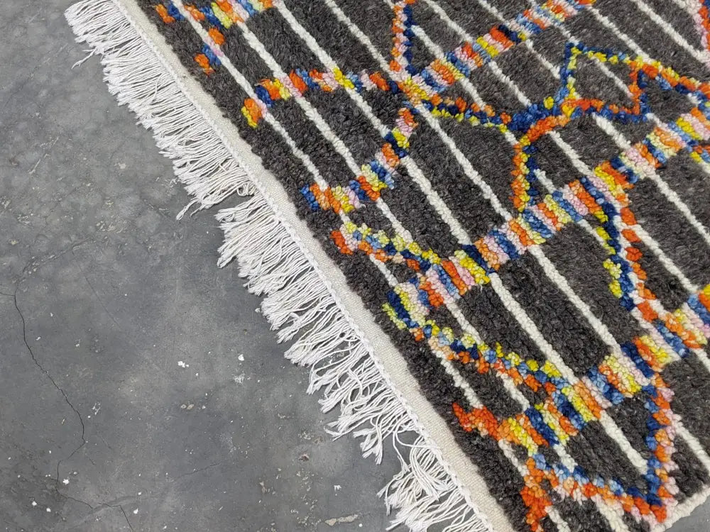 A vibrant moroccan handmade azilal rug in pure natural wool with dark gray base and bold geometric patterns by DecorBites