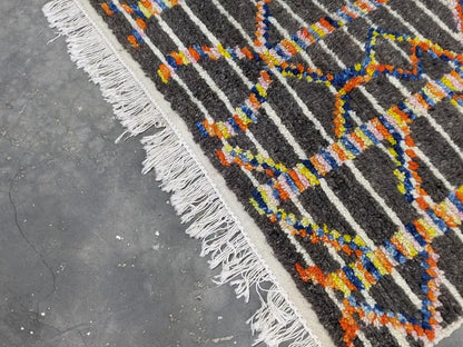 A vibrant moroccan handmade azilal rug in pure natural wool with dark gray base and bold geometric patterns by DecorBites