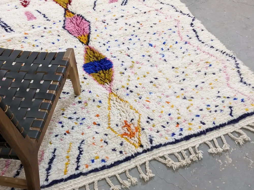 A fluffy white moroccan handmade traditional azilal rug with colorful geometric patterns and fringed edges by decorbites