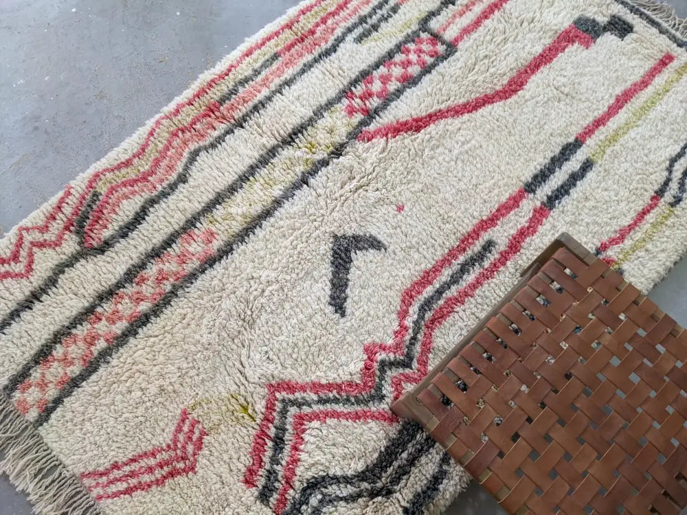 Cream-colored moroccan handmade traditional azilal rug with bold red and black geometric patterns by decorbites™