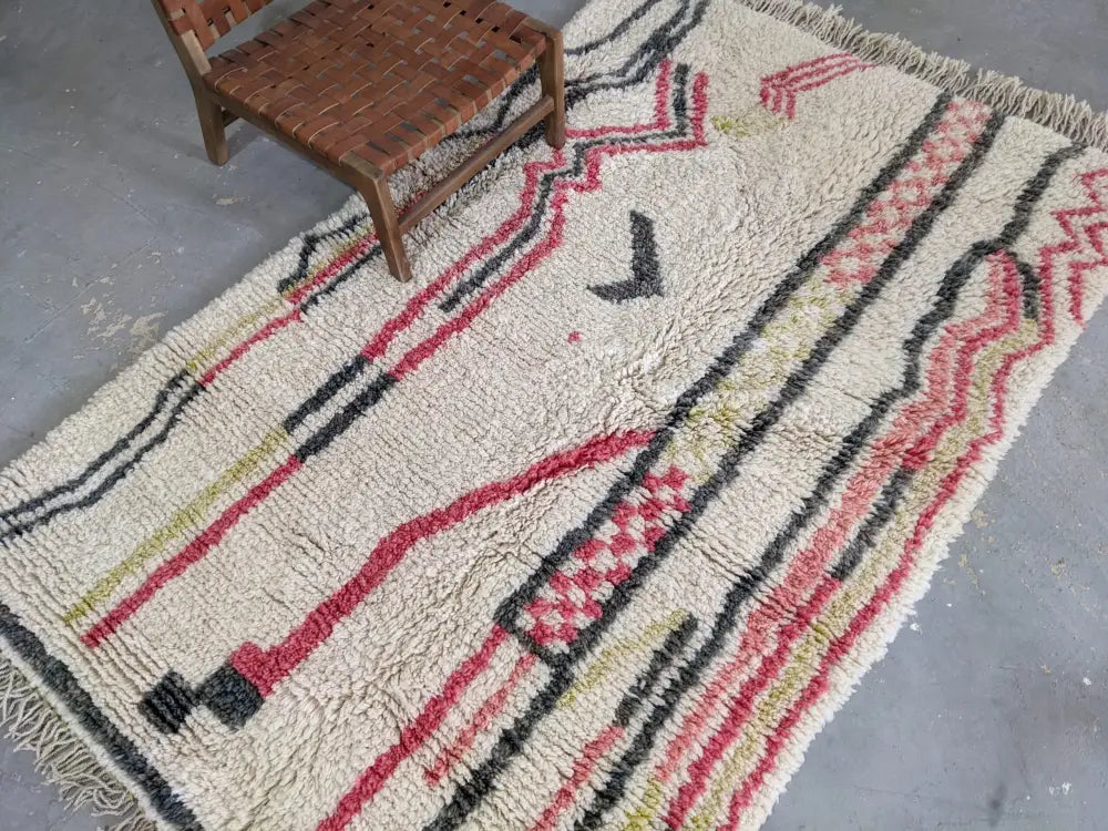 Cream-colored moroccan handmade traditional azilal rug with bold red black olive green geometric patterns and fringed edge
