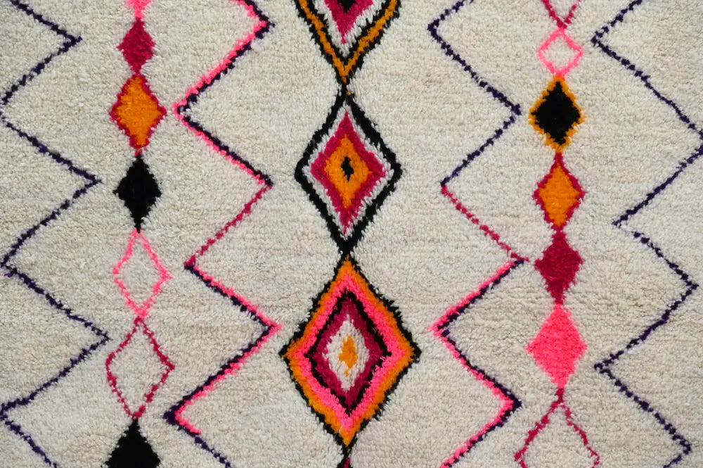 A moroccan handmade traditional azilal rug with bold pink orange and black geometric diamond patterns on an off-white plush surface