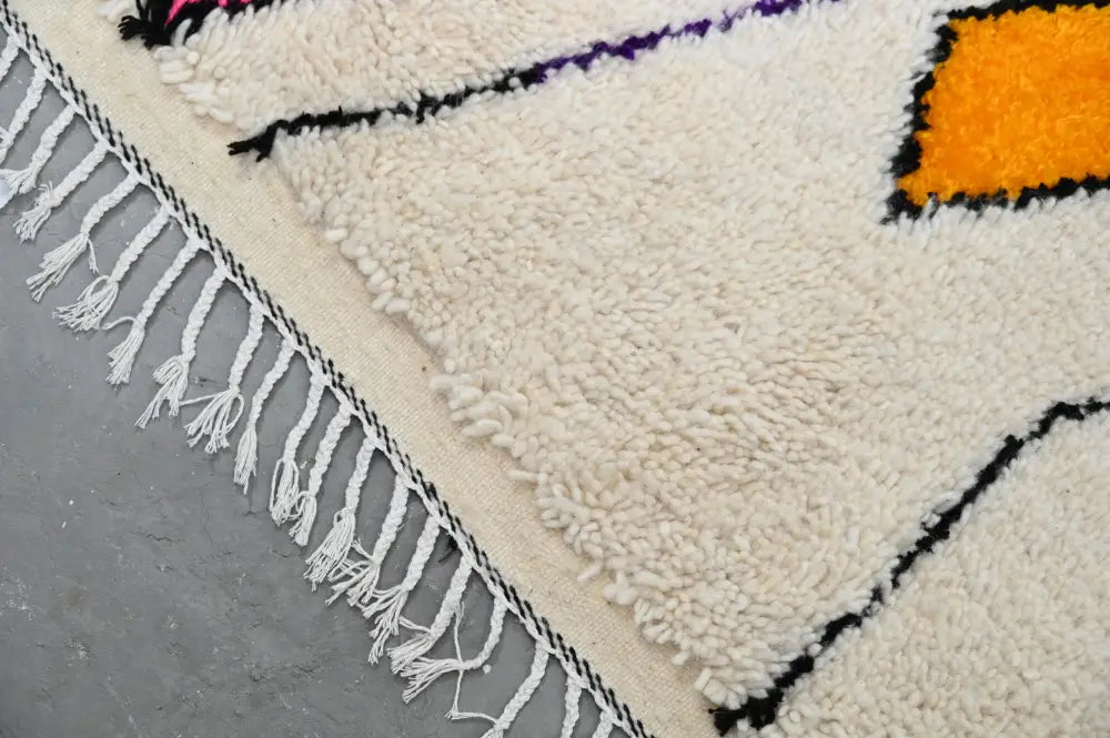 Cream-colored moroccan handmade traditional azilal rug with bold black orange and purple geometric patterns and fringed edge