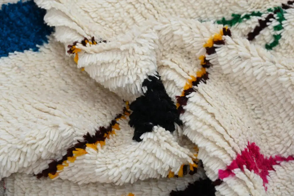 A cream-colored moroccan handmade traditional azilal rug with bold black blue yellow and pink geometric patterns by decorbites