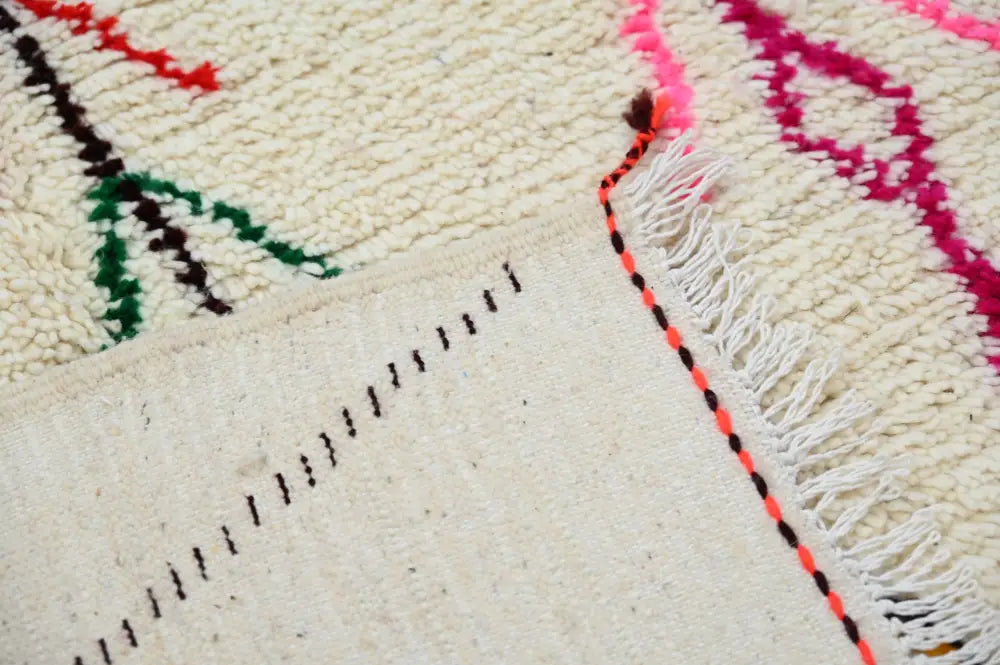 Cream-colored decorbites™ moroccan handmade traditional azilal rug with vibrant pink green black geometric patterns and fringed edge