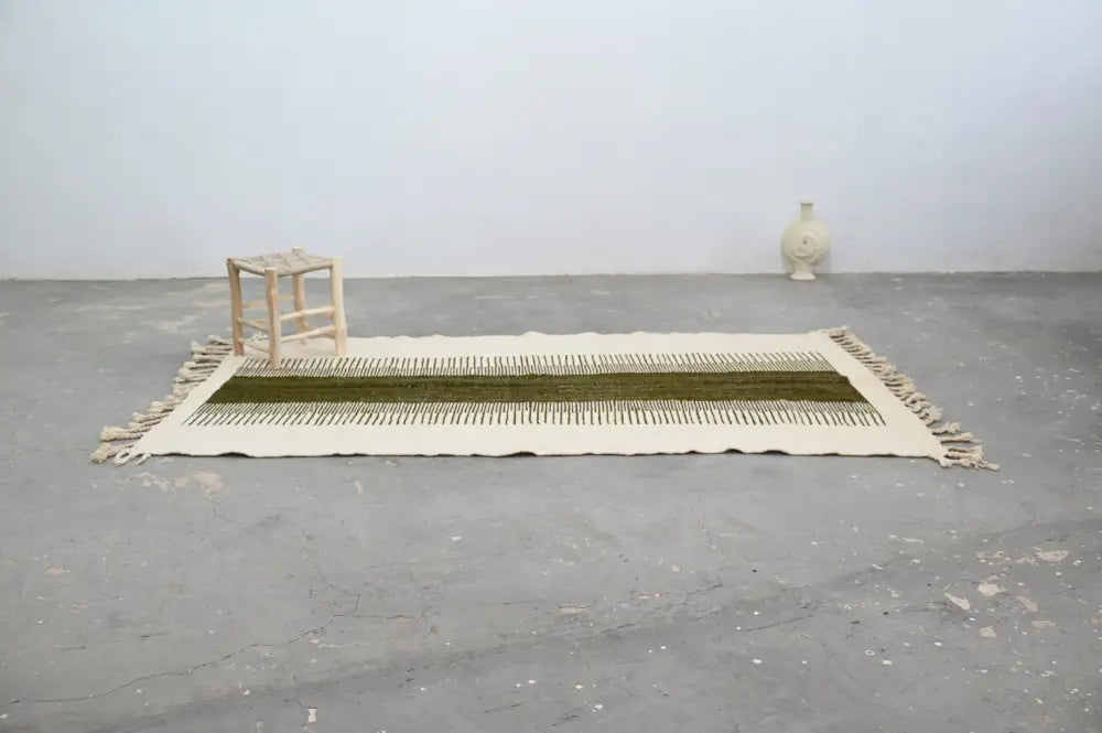 A cream-colored moroccan handmade traditional azilal rug with a central olive green stripe and fringed edges