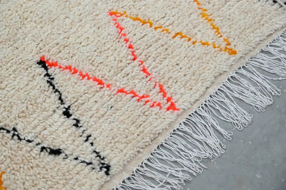 Cream-colored DecorBites™ moroccan handmade traditional azilal rug with bold orange black geometric patterns and white fringe