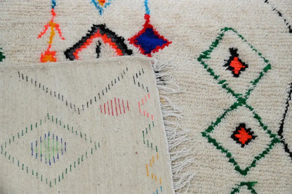 Cream-colored moroccan handmade traditional azilal rug with intricate geometric patterns and fringed edges by decorbites