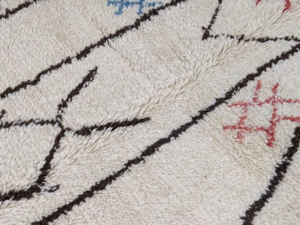 Cream-colored moroccan handmade azilal rug with plush texture bold black geometric lines and subtle blue pink details in pure natural wool