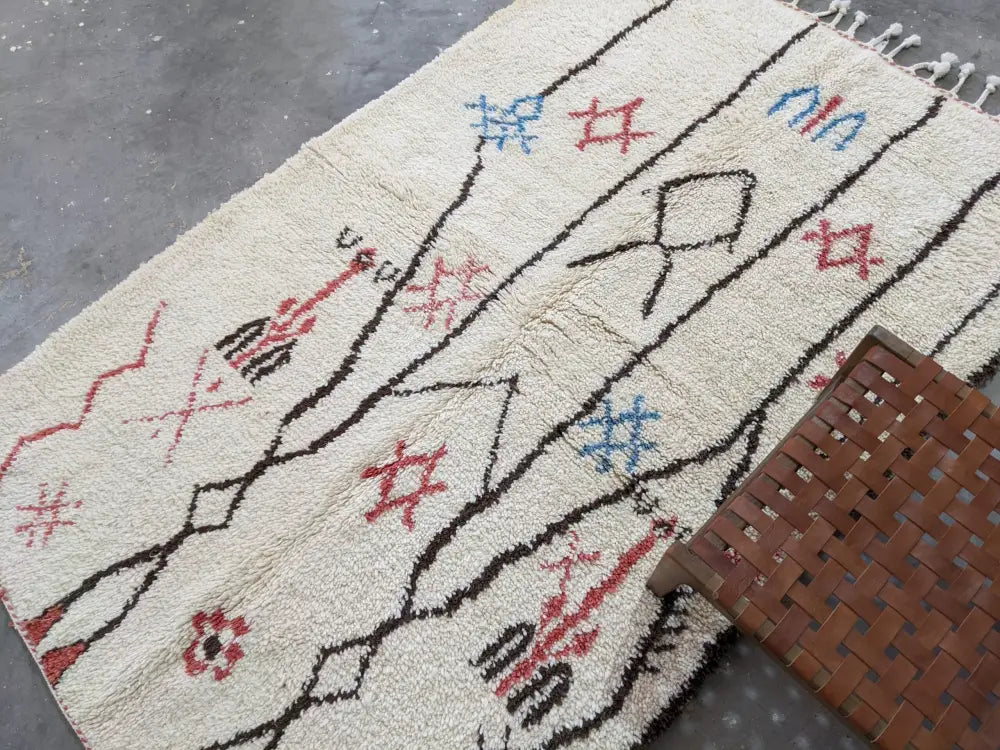 Cream-colored moroccan handmade azilal rug in pure natural wool with black red and blue geometric patterns and fringed edges