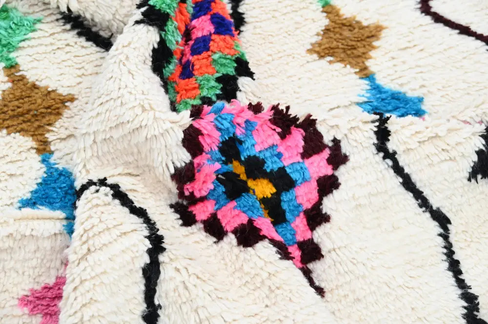 A plush cream-colored moroccan handmade traditional azilal rug with vibrant pink blue orange green and brown geometric patterns