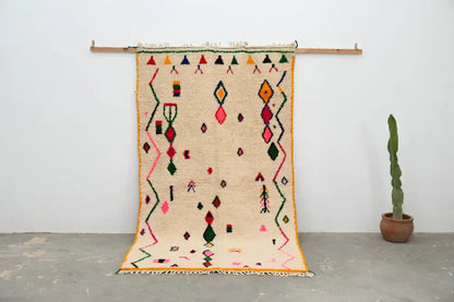 Beige moroccan handmade traditional azilal rug with vibrant pink green orange and red geometric patterns on woolen surface