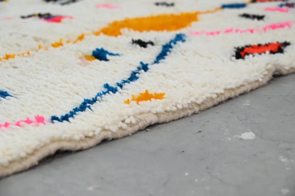 A fluffy white moroccan handmade traditional azilal rug with vibrant orange blue pink and black geometric patterns