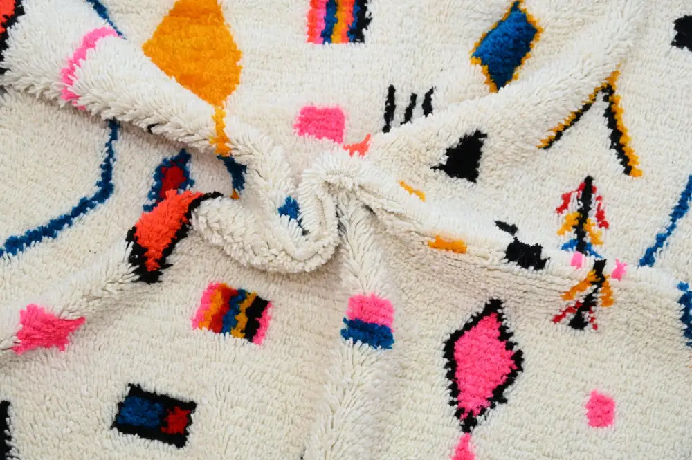 A plush off-white moroccan handmade traditional azilal rug with vibrant pink blue orange black and yellow geometric patterns