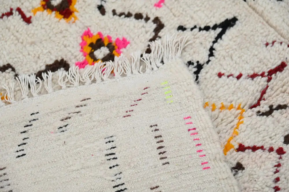 A cream-colored moroccan handmade traditional azilal rug with vibrant geometric patterns and a textured hand-knotted weave