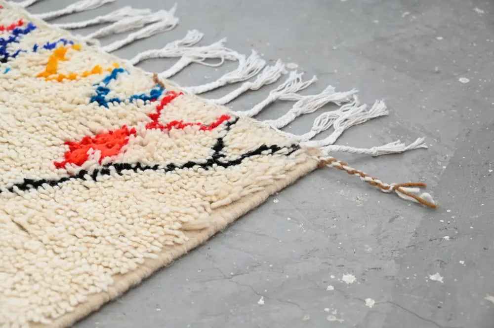 Cream-colored moroccan handmade traditional azilal rug with vibrant red blue yellow patterns and long white fringe by DecorBites