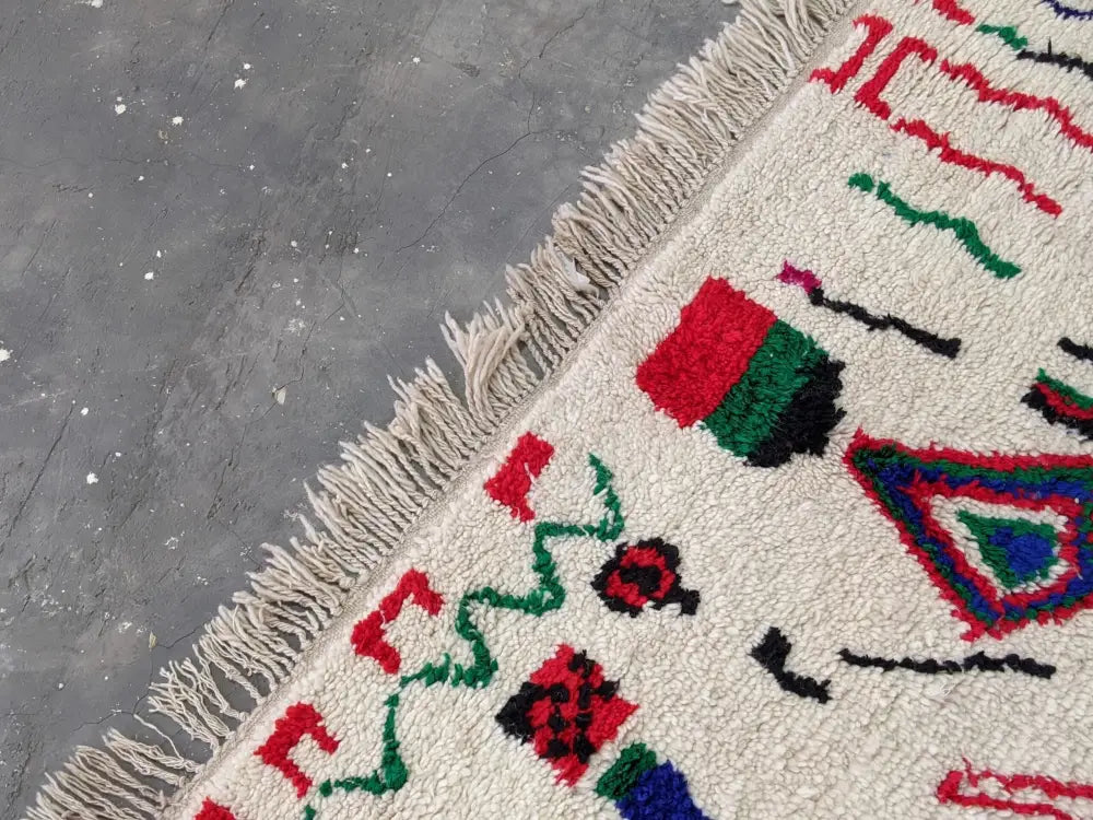 Cream-colored moroccan handmade azilal rug with vibrant red green blue patterns and thick fringe in pure natural wool