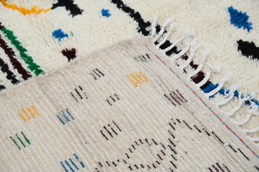 Cream-colored wool moroccan handmade traditional azilal rug with intricate geometric patterns and fringed edge
