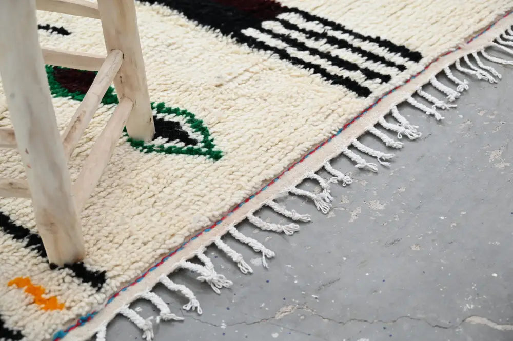 Cream-colored moroccan handmade traditional azilal rug with black green orange geometric patterns and fringed edge 273 x 155 cm