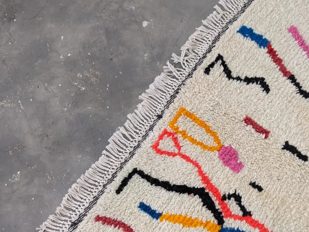 Cream-colored moroccan handmade azilal rug with vibrant geometric patterns and thick fringed edges in pure natural wool