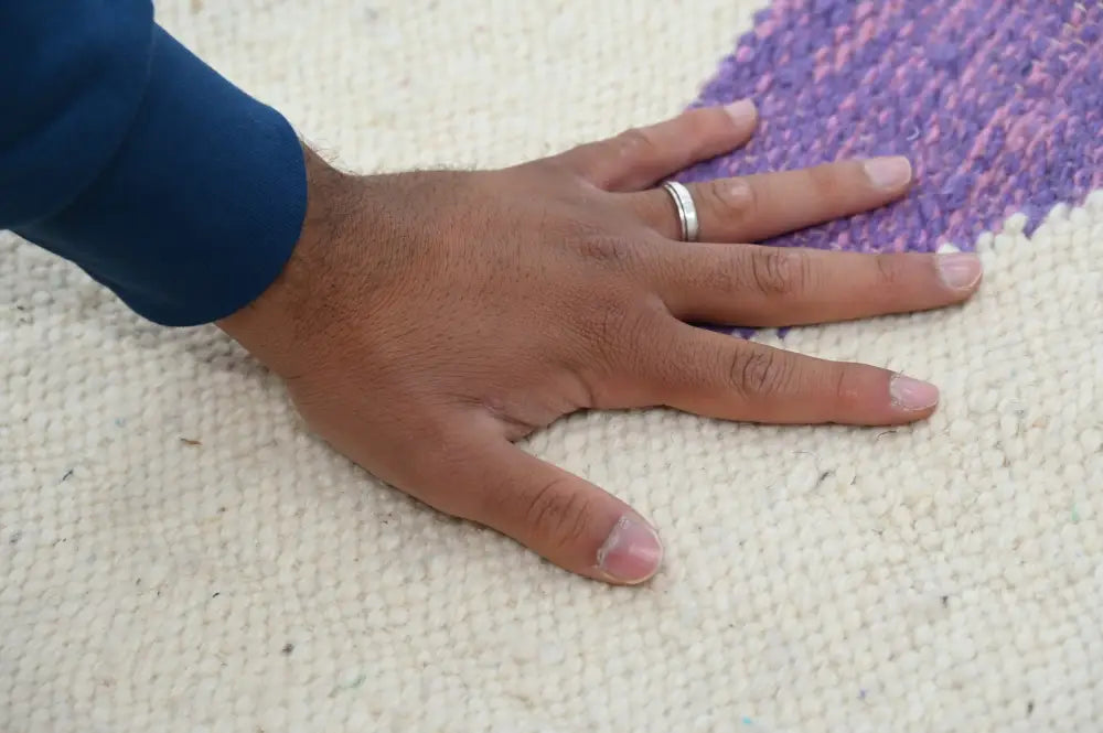 A hand with a silver ring rests on a moroccan handmade traditional azilal rug with vibrant purple and pink border