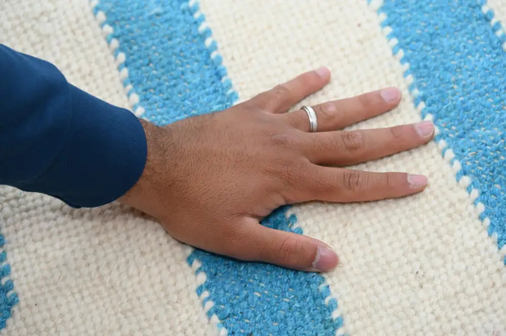 A hand with a silver ring rests on a blue and cream moroccan handmade traditional azilal rug by DecorBites