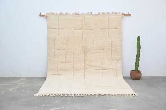 Beige moroccan handmade beni ouarain carpet with geometric pattern and fringed edges hanging on wooden rods