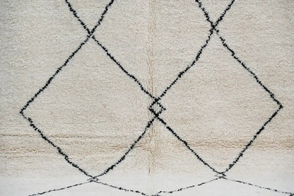 Cream-colored moroccan handmade beni ouarain carpet with textured fluffy surface and bold black geometric diamond patterns