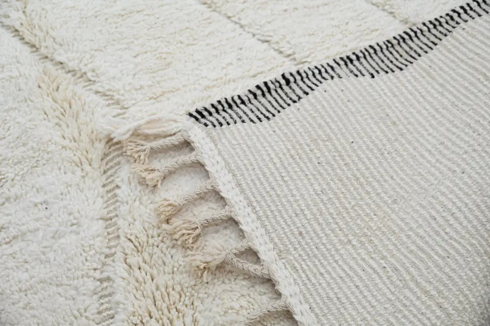 Cream-colored beni ouarain rug with black geometric stitching and textured fringed edge moroccan handmade wool decor