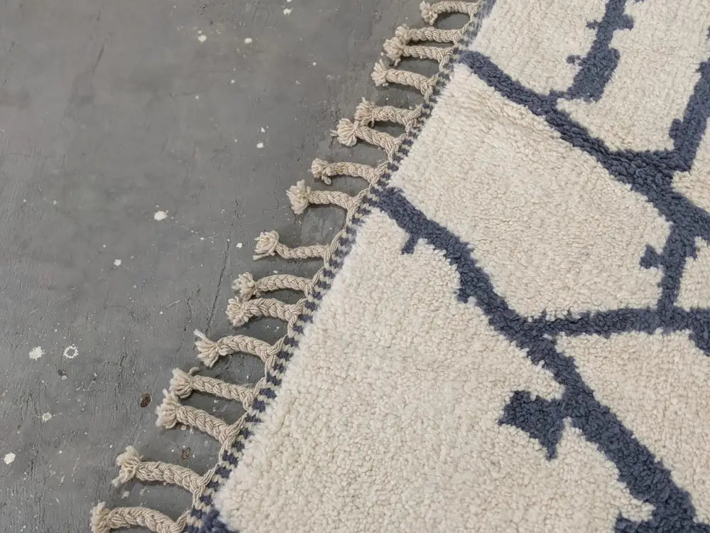 Cream-colored beni ouarain rug with navy blue geometric patterns and fringed edge moroccan handmade traditional design