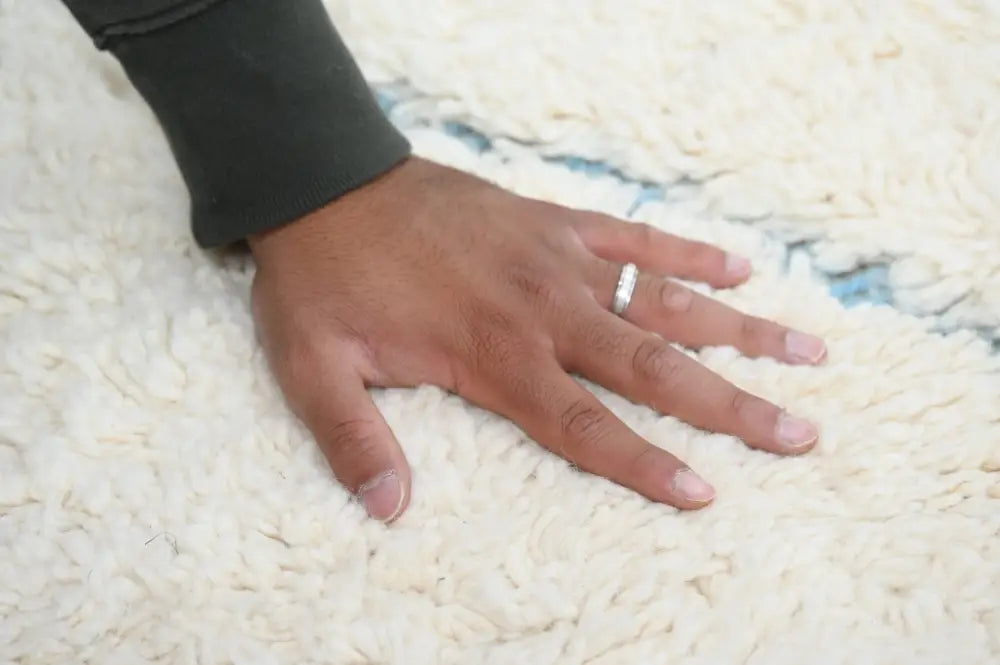 A hand with a silver ring rests on a plush off-white Moroccan handmade beni ouarain rug by DecorBites