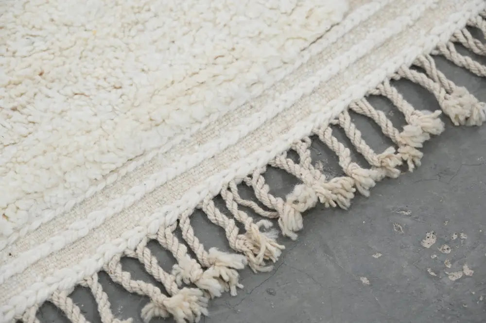 Cream-colored plush moroccan handmade beni ouarain rug with textured surface and braided fringe 300 x 208 cm
