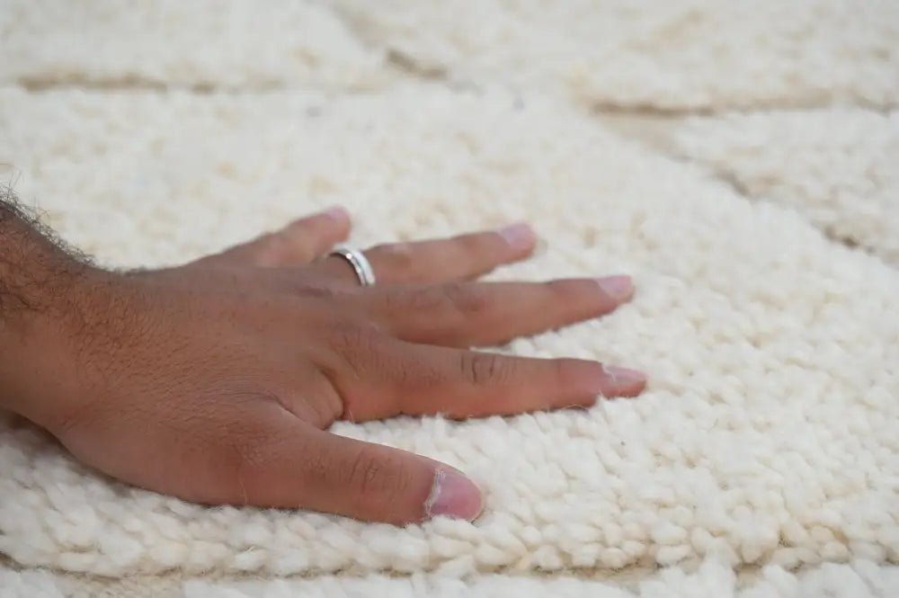 A hand with a silver ring rests on a plush off-white moroccan handmade beni ouarain rug by decorbites