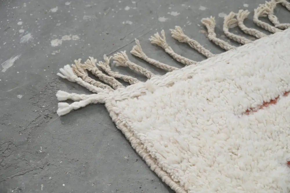 Cream-colored moroccan handmade beni ouarain rug with chunky wool texture fringed edges and subtle reddish-orange stripe