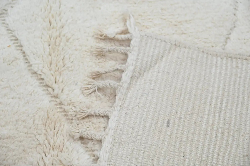 Cream-colored moroccan handmade beni ouarain rug with textured surface and fringed edges 302 x 200 cm by DecorBites