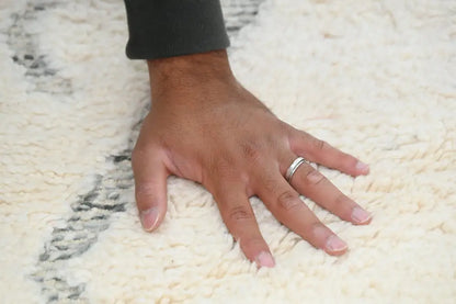A hand with a silver ring rests on a cream-colored moroccan handmade beni ouarain rug with black geometric patterns