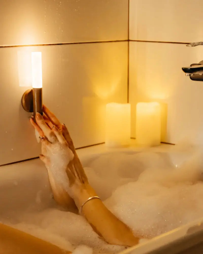 A hand holding a sleek cylindrical decorbites moroccan rechargeable battery-operated wall sconce with warm glow