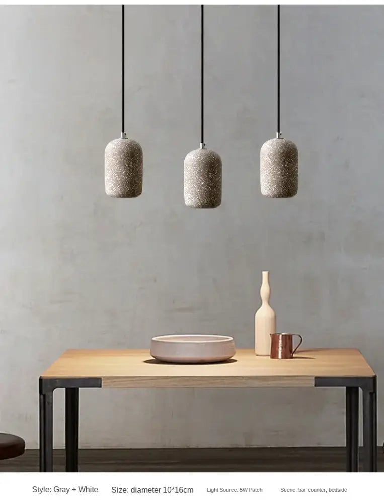 Three gray and white speckled cement pendant lamps with black cords in industrial style lighting by DecorBites™